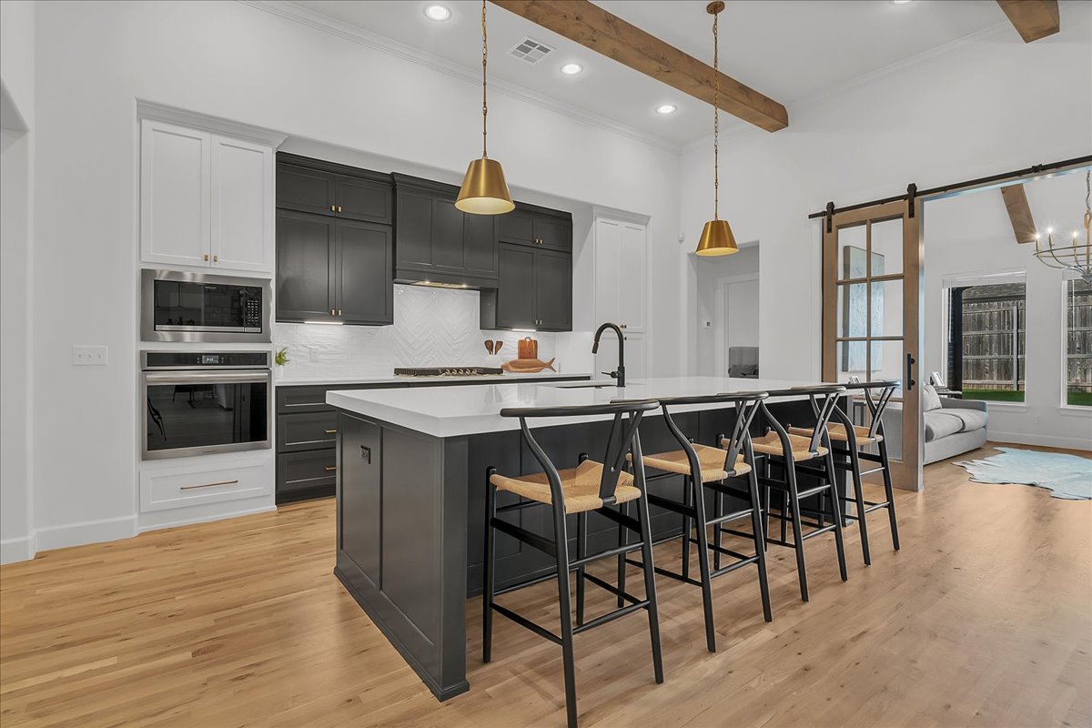 Kitchen with dark cabinets, a large island with bar seating, gold pendants, and exposed wood ceiling beams.