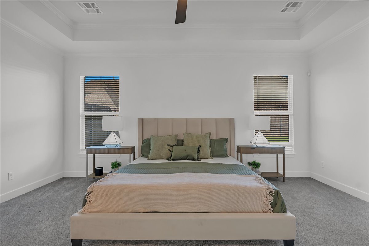 Staged bedroom with a centered upholstered bed, matching bedside tables, and windows with blinds.
