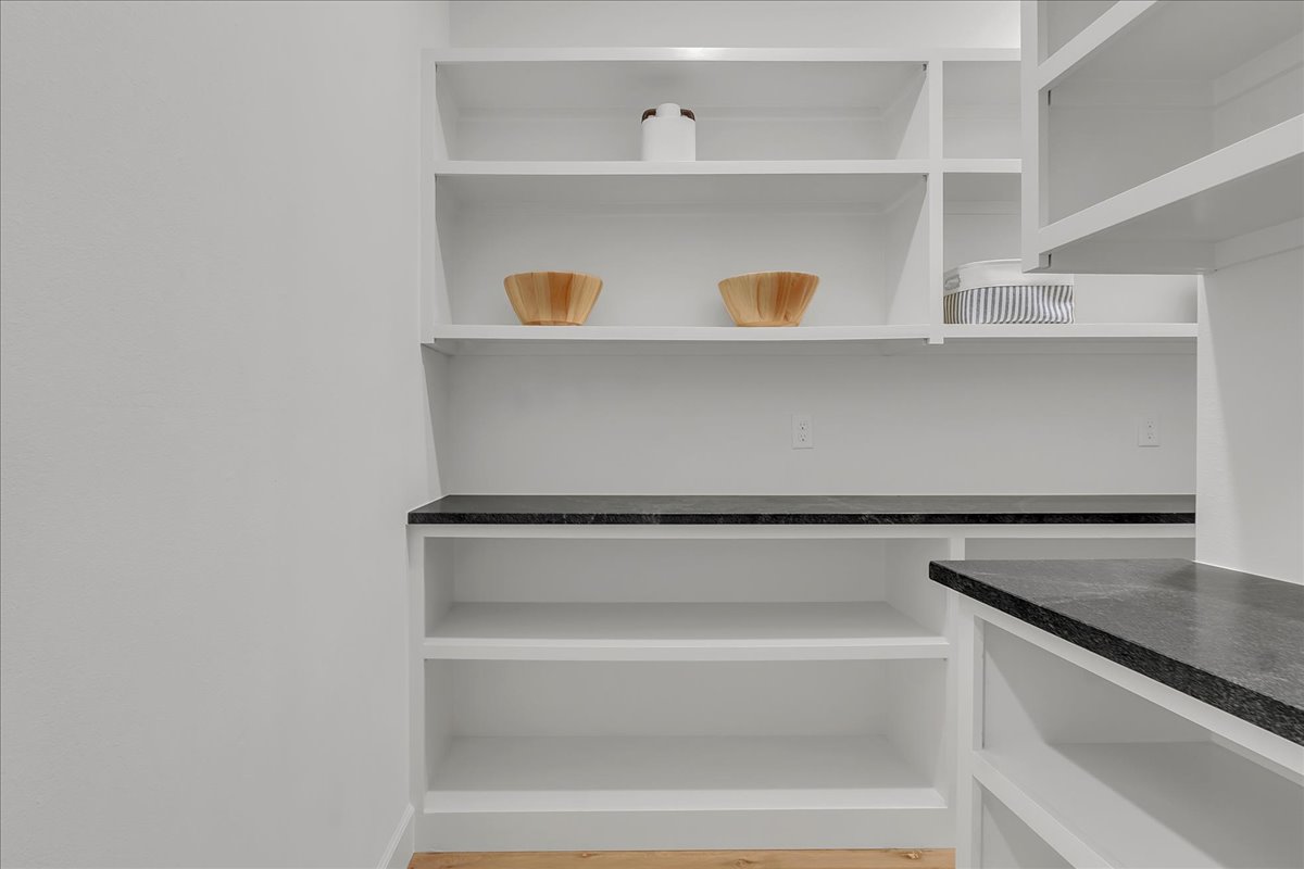 Pantry with white open shelving, dark stone counters, and decorative bowls