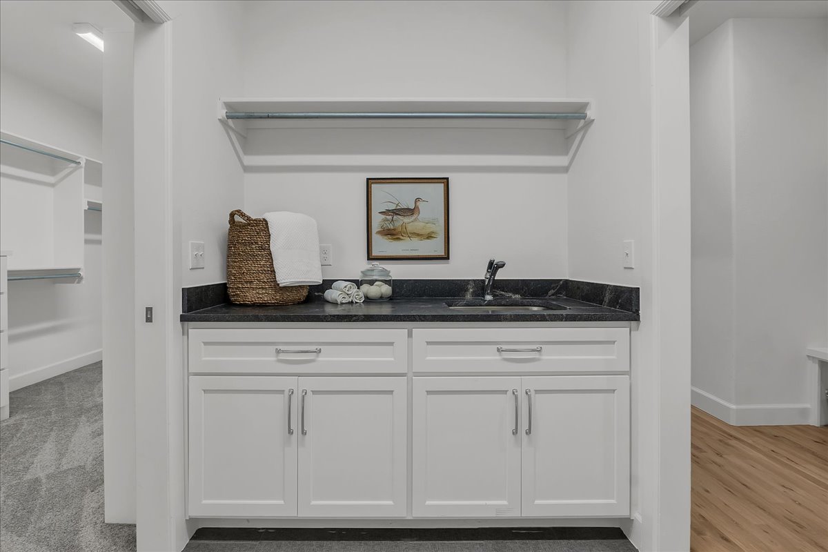 Bathroom vanity with a black countertop, white cabinetry, and framed bird print.