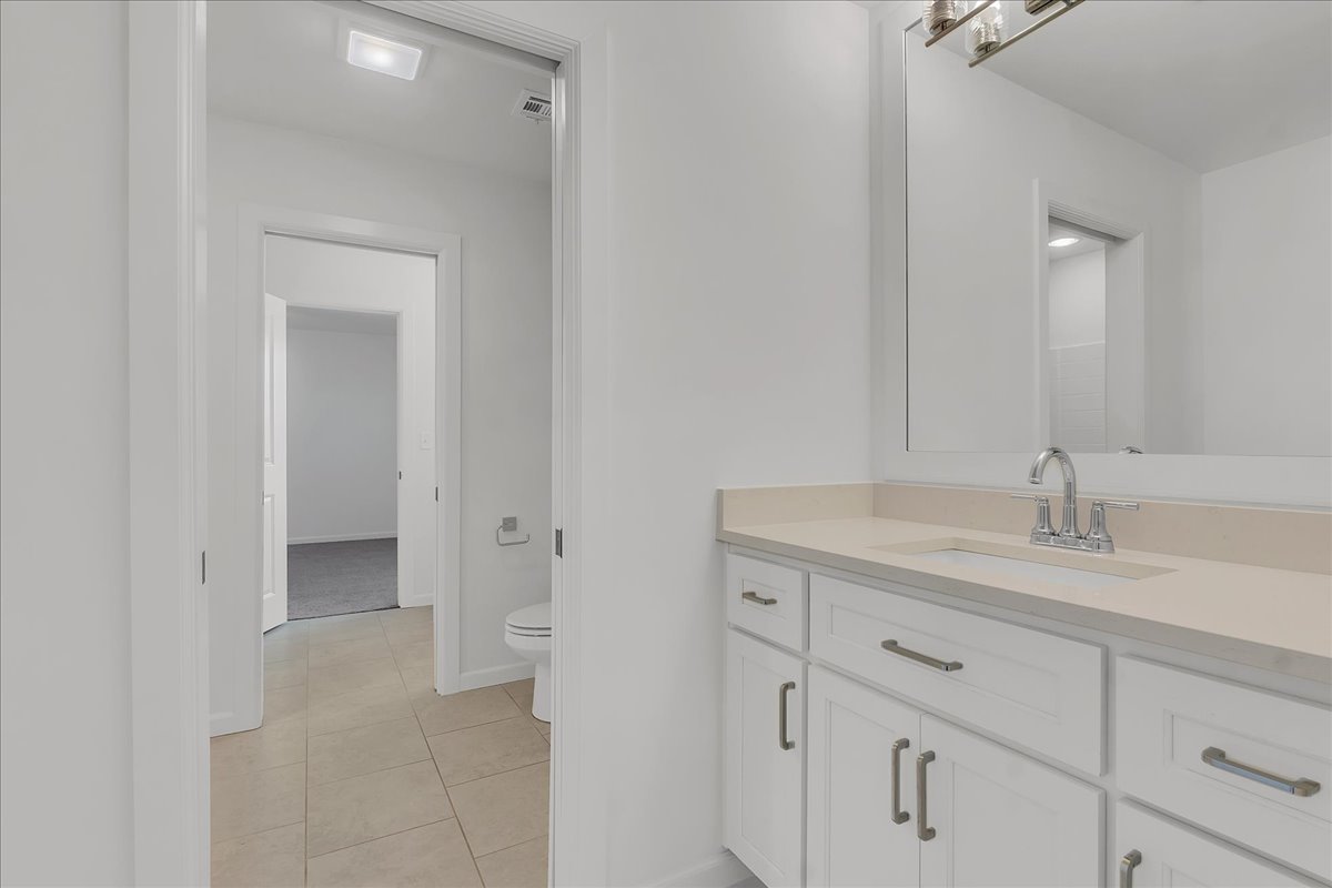 Bathroom with a long white vanity, large mirror, and beige tile floor.