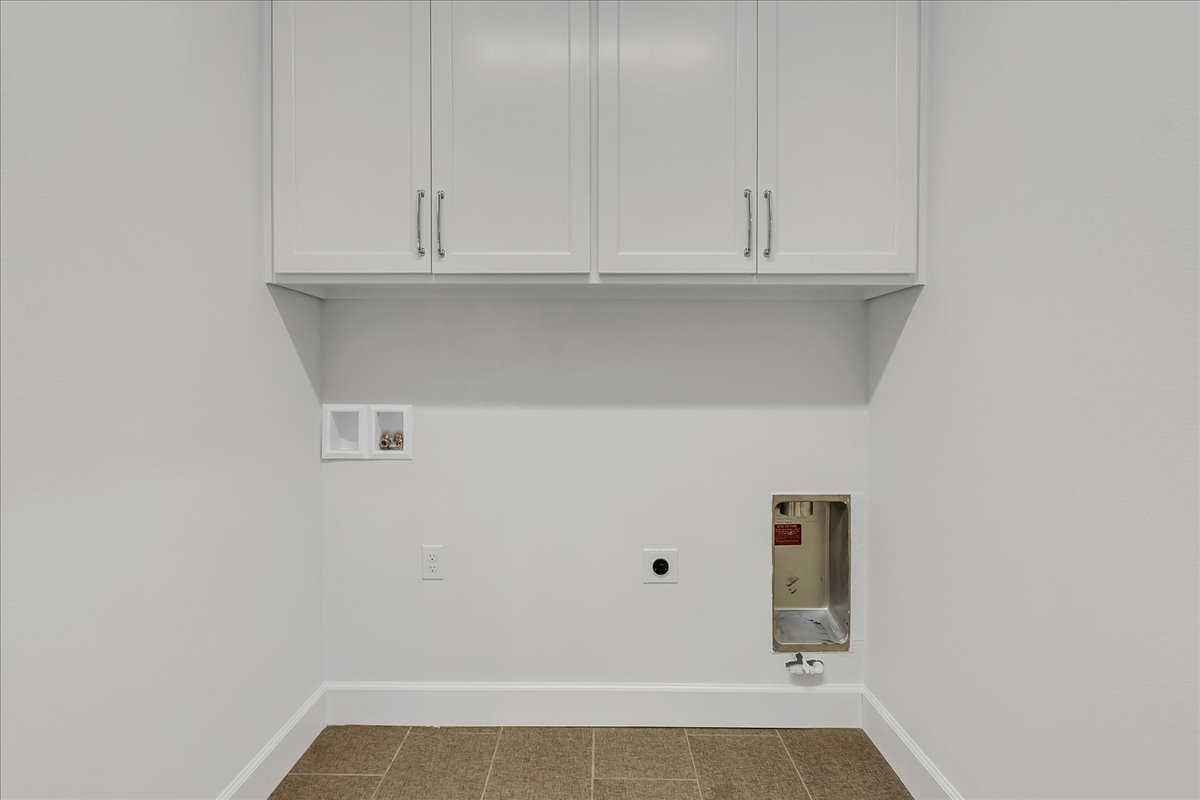 Empty laundry area with white cabinets, washer and dryer hookups, and brown tile flooring.