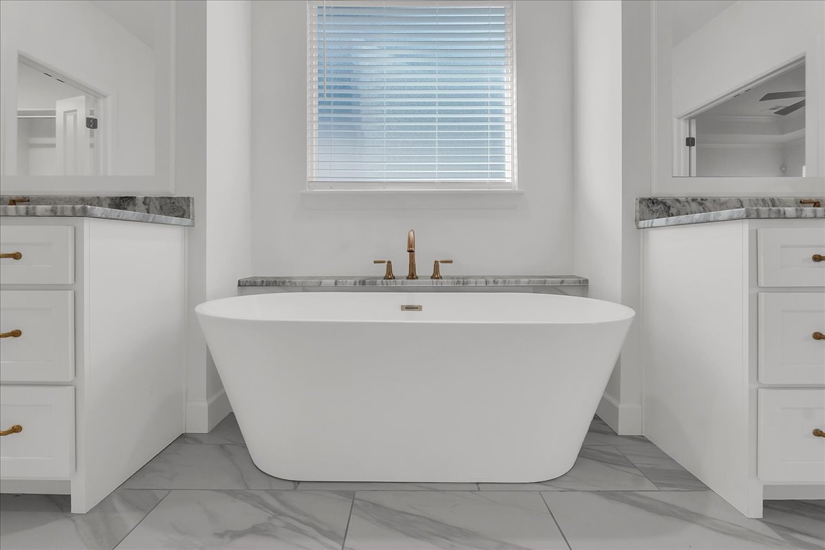Primary bathroom with a freestanding soaking tub, marble-look counters, and brass fixtures.