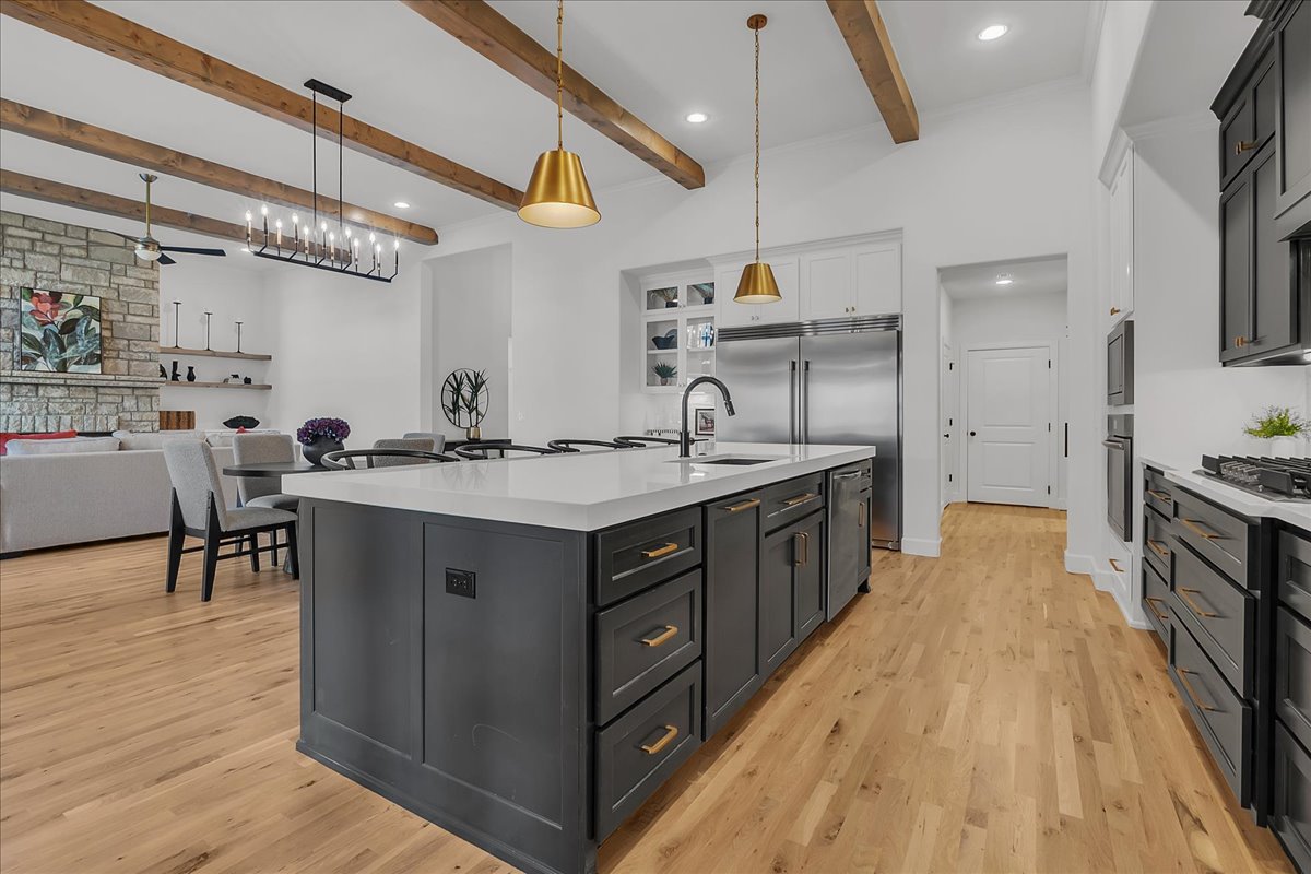 Open kitchen with a large charcoal island, stainless steel appliances, and exposed wood ceiling beams.