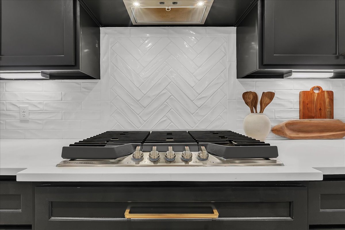 Kitchen gas cooktop beneath a white herringbone tile backsplash, framed by dark cabinetry.