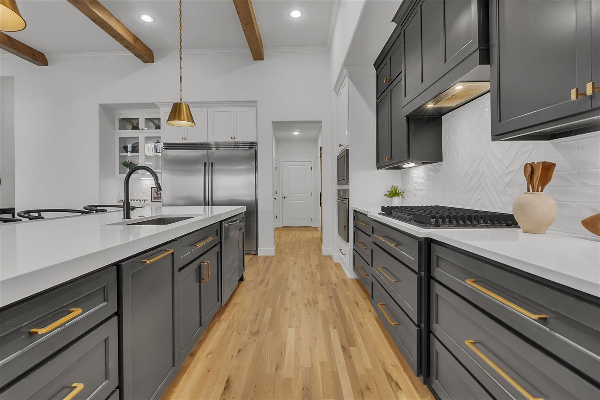 Renovated kitchen with dark gray cabinets, brass hardware, a large island, and exposed wood ceiling beams.