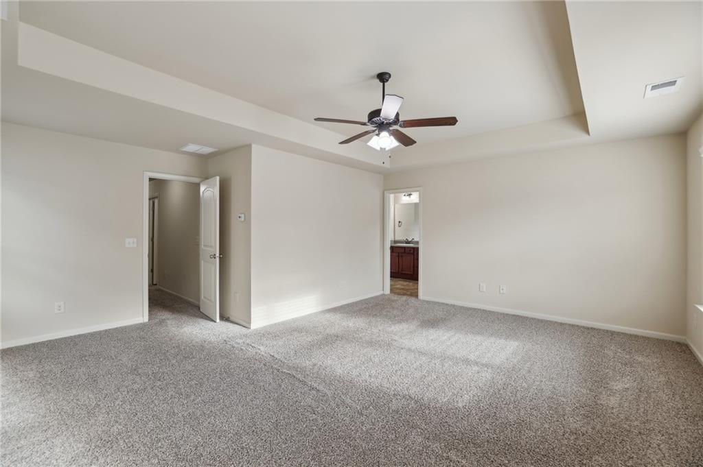 Empty carpeted bedroom with a ceiling fan and an open doorway to the bathroom.