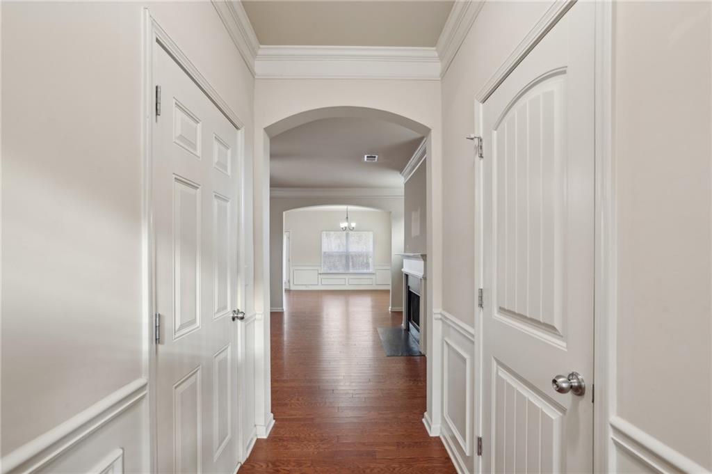Vacant hallway with hardwood floors, paneled doors, and an arched opening toward a fireplace.