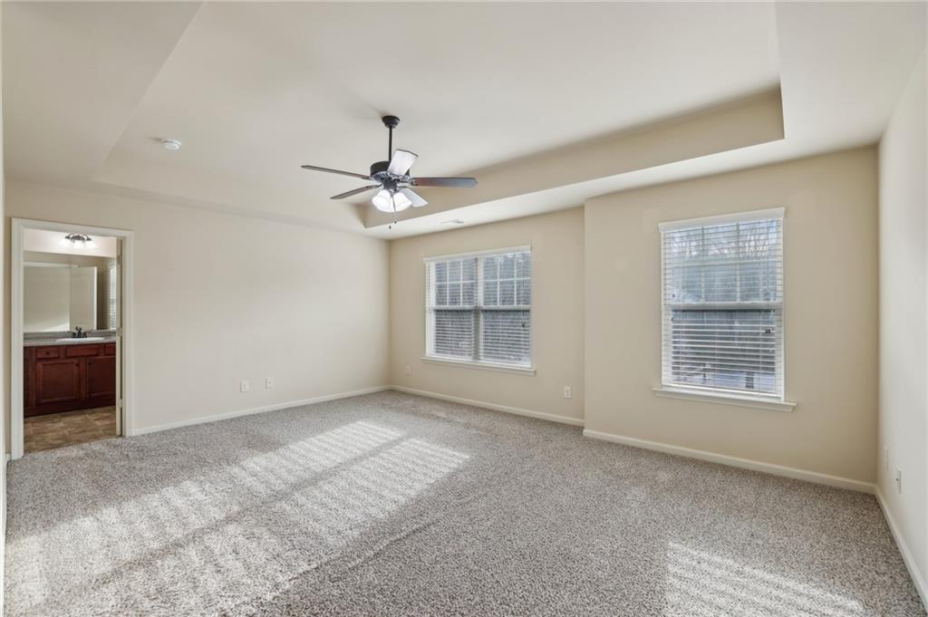 Vacant bedroom with a tray ceiling, ceiling fan, gray carpet, and two windows.