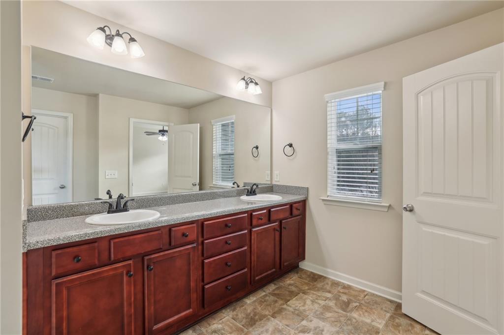 Bathroom with a double-sink vanity, reddish-brown cabinetry, large mirror, and window with blinds.