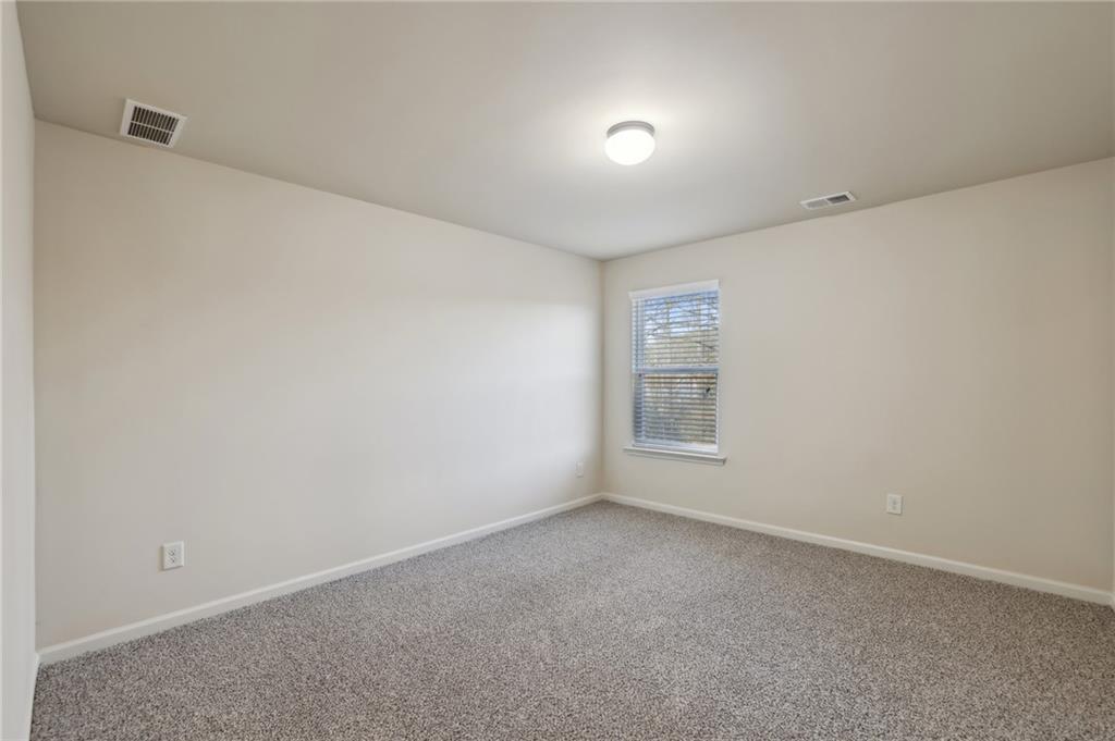 Empty bedroom with gray carpet, beige walls, and a window with blinds.