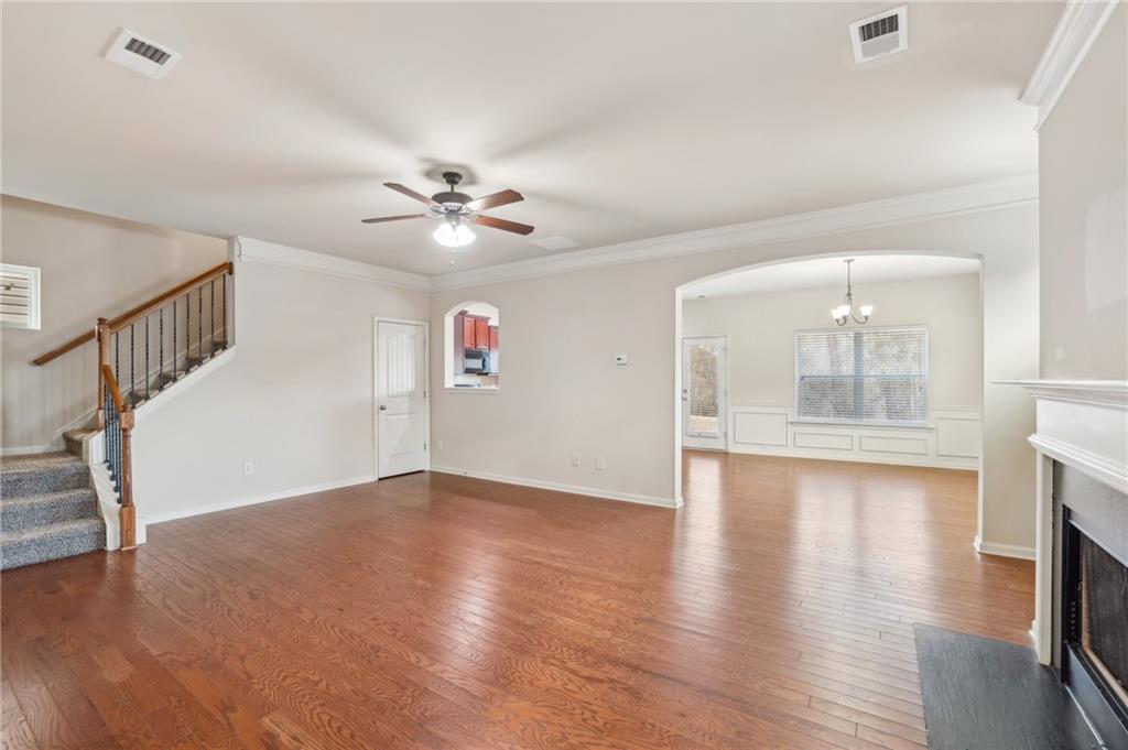 Vacant living room with hardwood floors, staircase, ceiling fan, and fireplace.