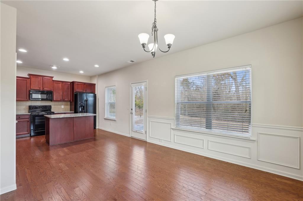 Dining area with hardwood floors, paneled walls, and an open kitchen with reddish wood cabinets.