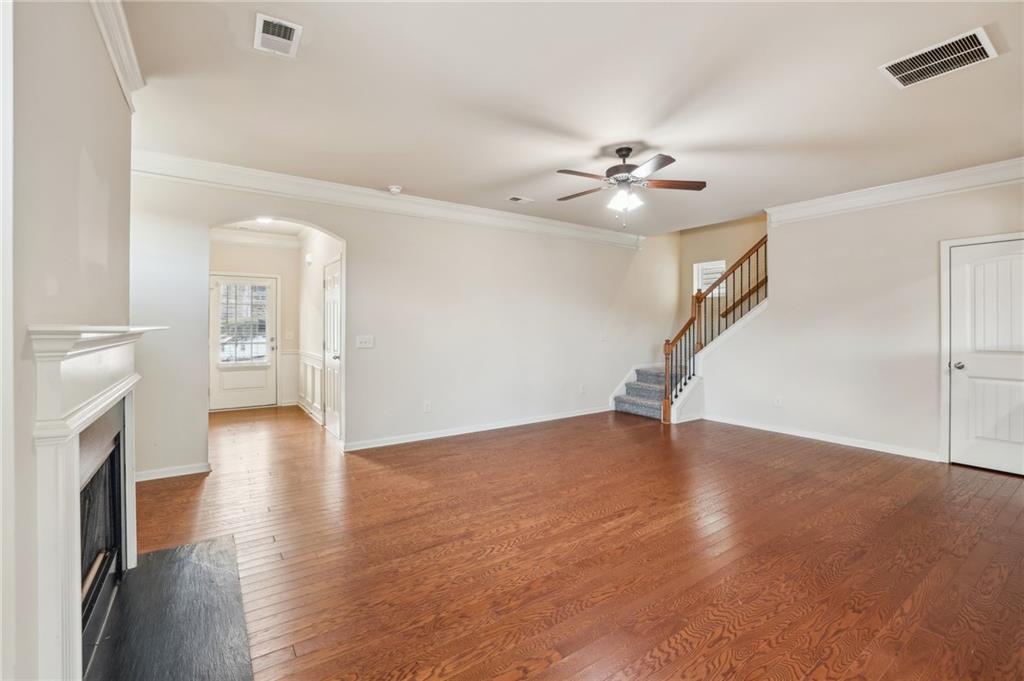 Empty living room with hardwood floors, a white fireplace, and a staircase with a wood railing.