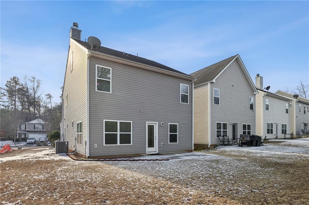 Rear of a gray two-story home with white trim, a small patio, and a lightly snow-covered lawn.