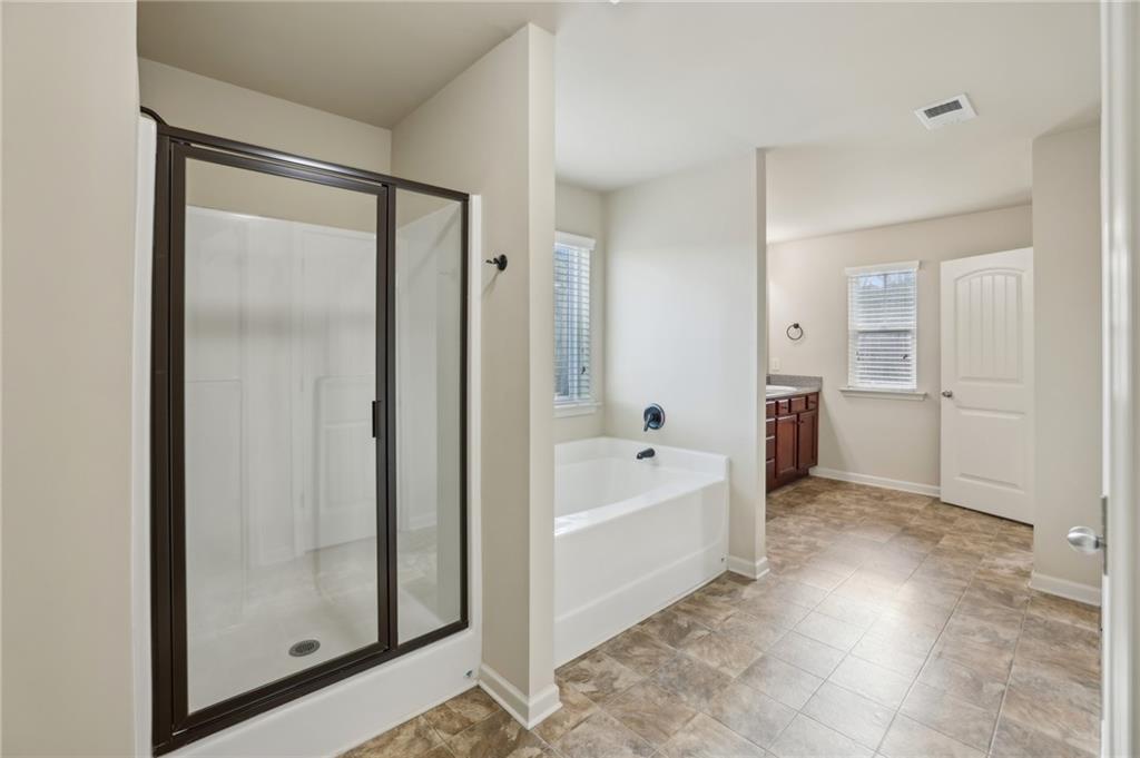 Bathroom with a glass-enclosed shower, soaking tub, wood vanity, and patterned tile floor.