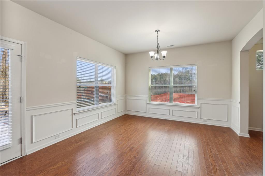 Empty dining room with hardwood floors, paneled wainscoting, and large windows.
