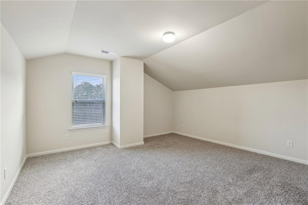 Empty carpeted room with a sloped ceiling and a window with blinds.