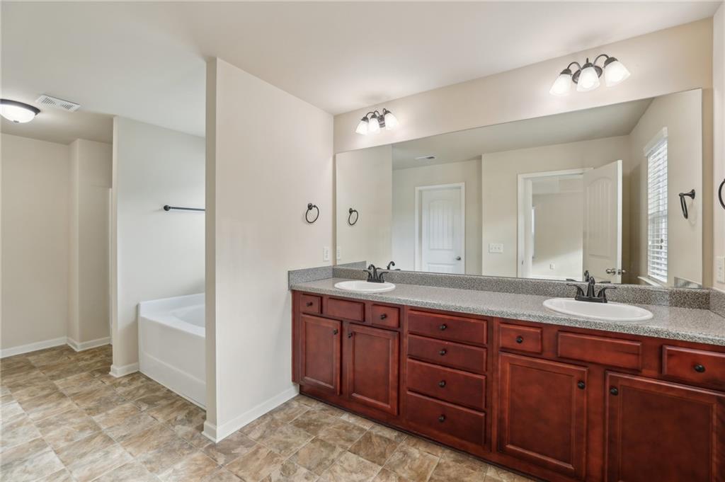 Bathroom with a double-sink wood vanity, large mirror, bathtub, and mottled tile floor.