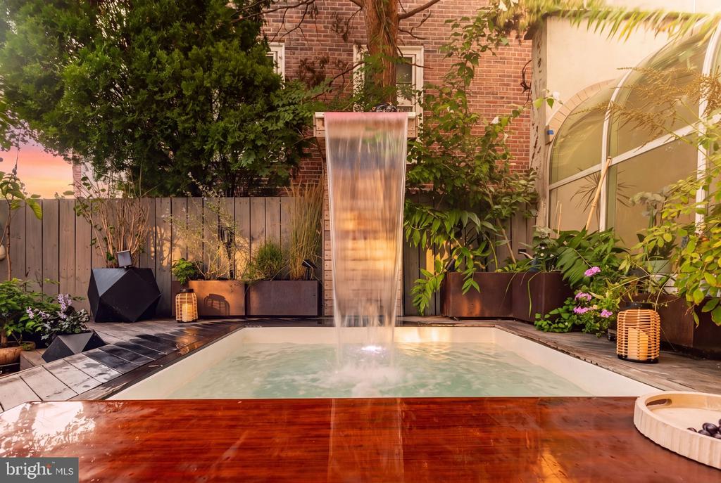 Courtyard pool and spa with a cascading waterfall, wooden deck, and surrounding planters.