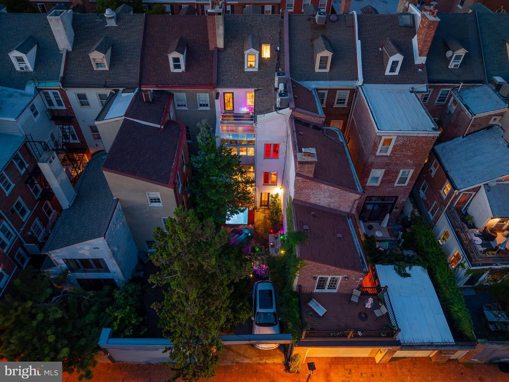 Aerial view of a Philadelphia rowhouse at dusk, with glowing windows and a leafy rear patio.