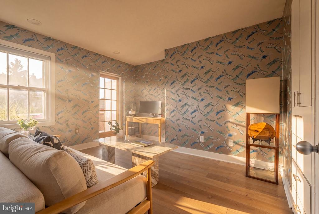 Living room with bird-patterned wallpaper, beige sofa, marble coffee table, and sunlit wood floors.