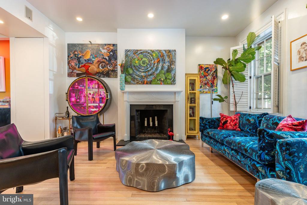 Living room with a fireplace, colorful artwork, blue patterned sofa, and leather chairs.