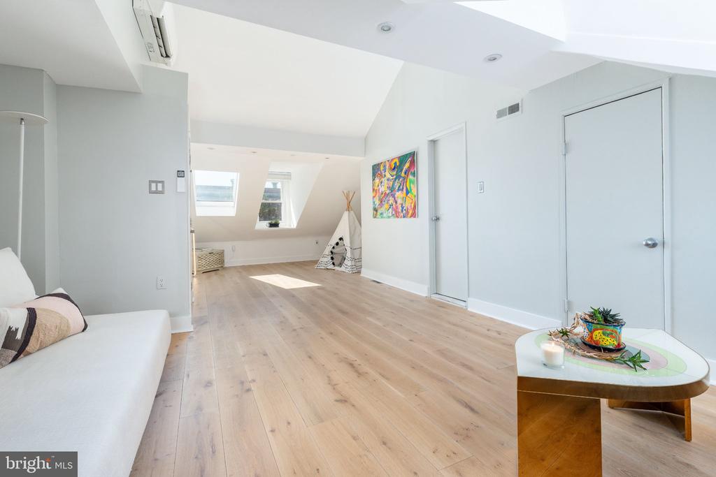 Bright living room with skylights, pale wood floors, colorful wall art, and a small teepee.