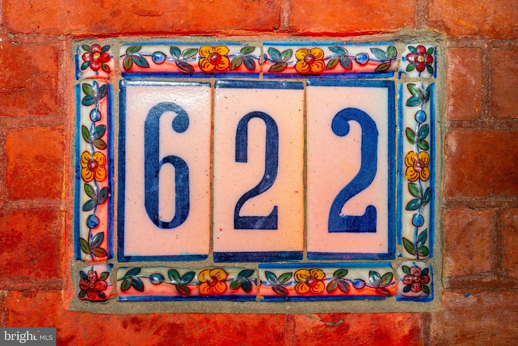 Ceramic 622 address plaque with a colorful floral border on a red brick wall.