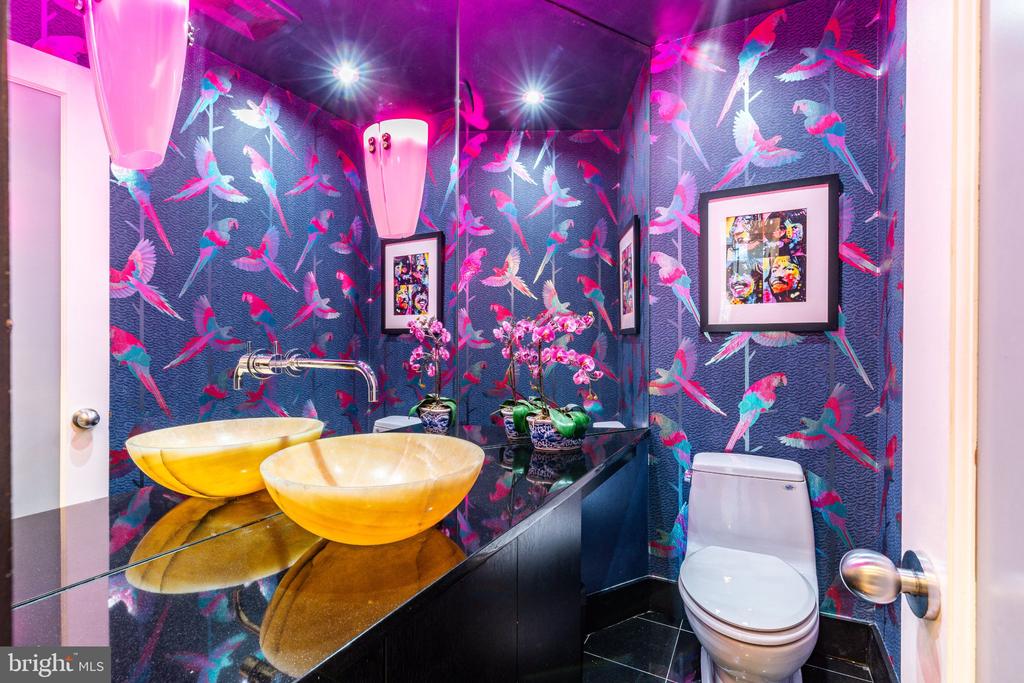 Powder room with bird-and-floral wallpaper, golden vessel sinks, a black vanity, and pink pendant lights.
