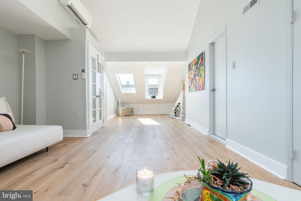 Attic living room with pale wood floors, skylights, colorful art, and a white sofa.