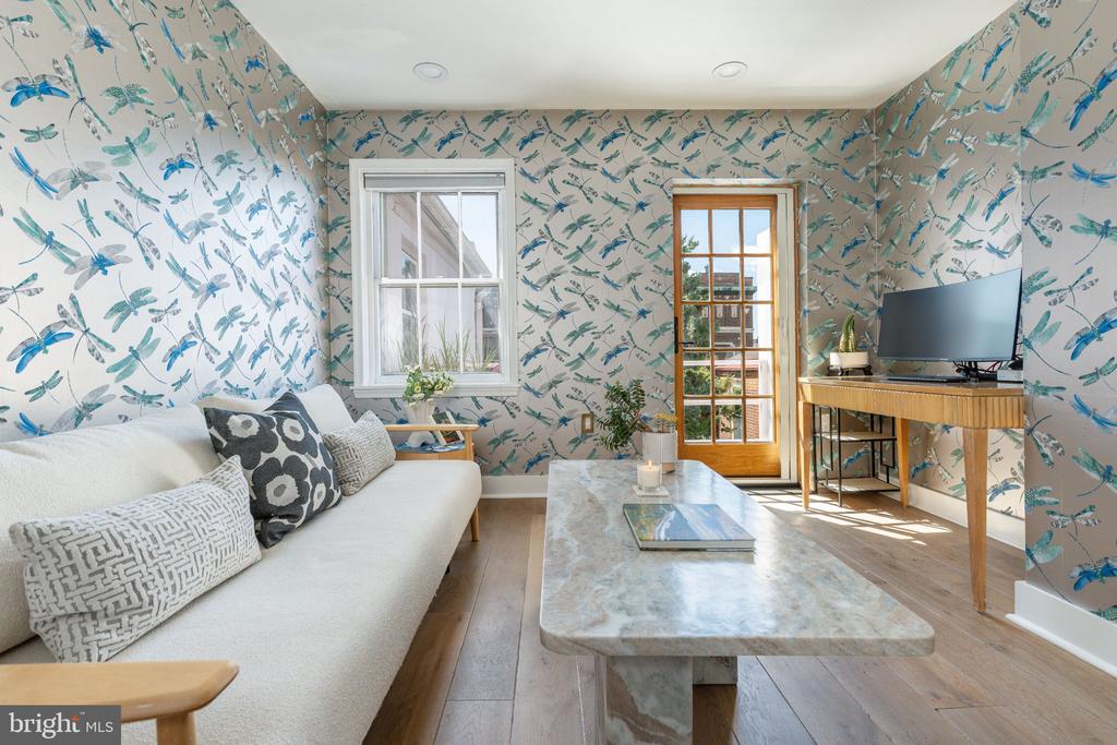 Living room with bird-patterned wallpaper, a white sofa, marble coffee table, and glass-paneled door.