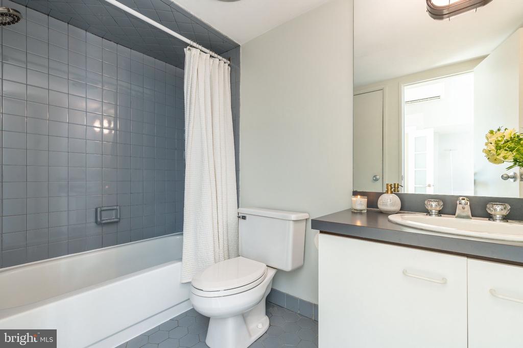 Bathroom with blue-gray tiled tub surround, white shower curtain, toilet, and dark-countertop vanity.