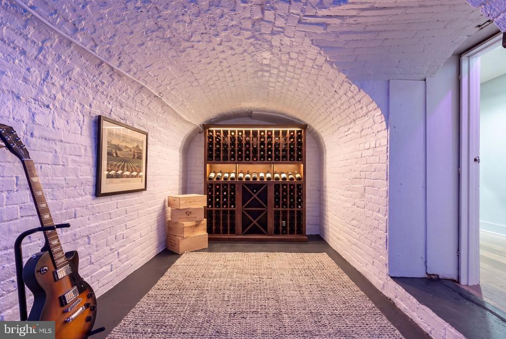 Wine cellar with vaulted brick walls, stocked wine racks, and a guitar.