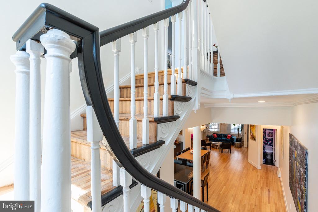 Hardwood staircase with white balusters and a dark curved handrail overlooking the living and dining areas.