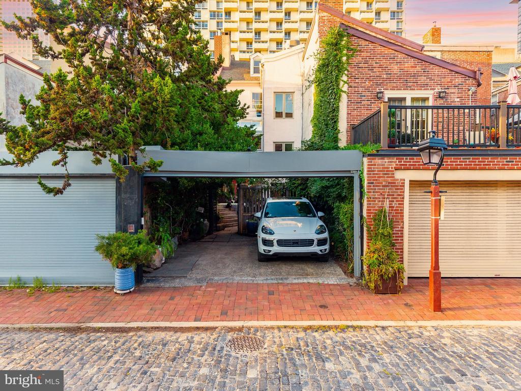 Brick residence with a covered driveway, white SUV, garage door, and upper-level balcony.