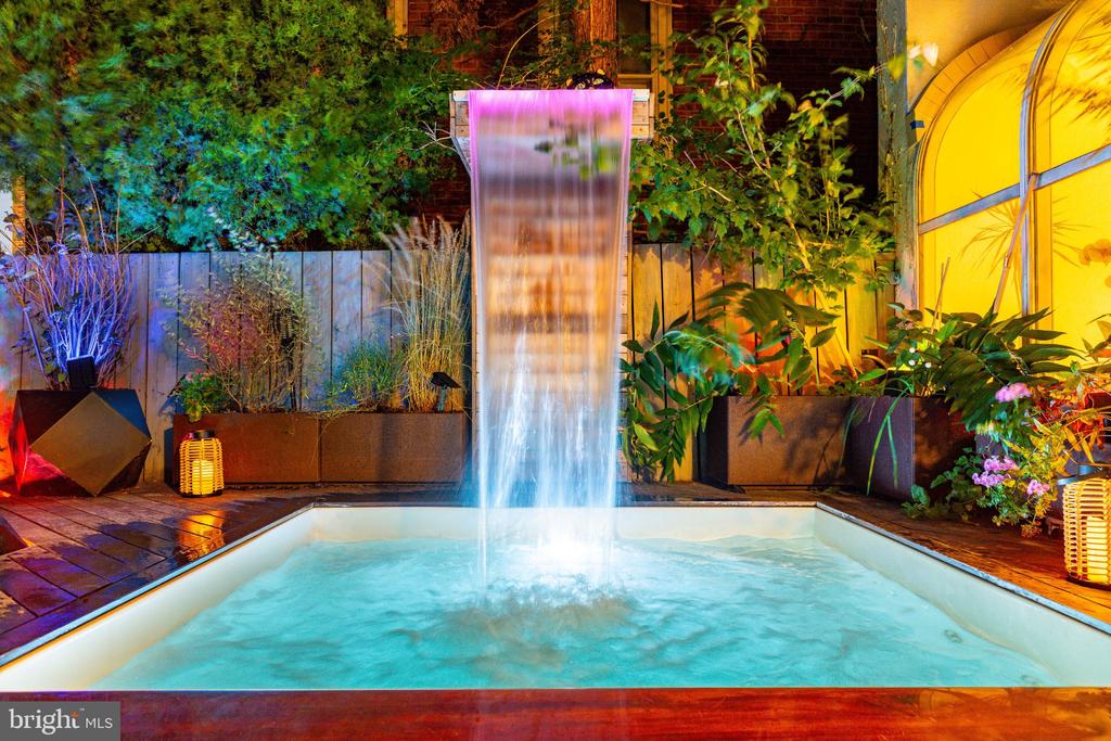 Outdoor pool with a tall waterfall, surrounded by planters and colorful nighttime lighting.