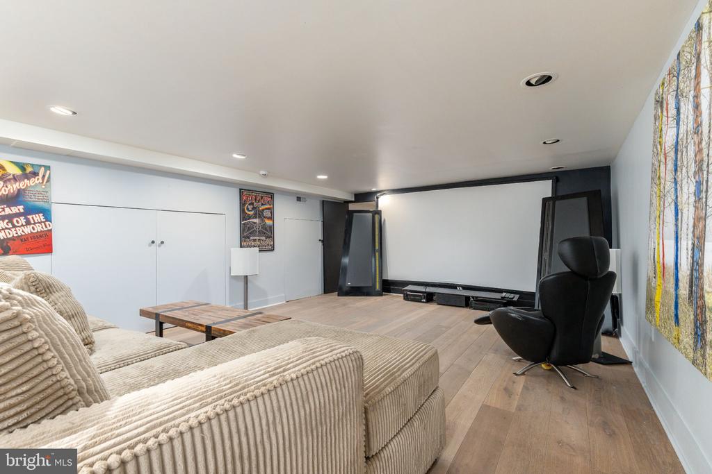 Furnished home theater with a large projection screen, black recliner, and cream sectional sofa.