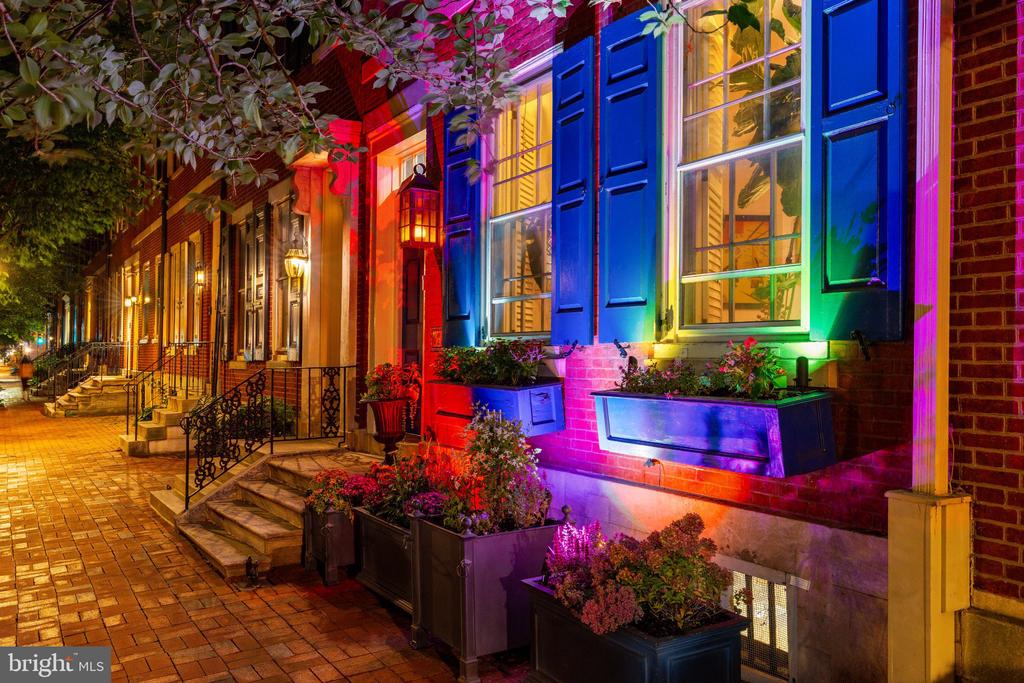 Brick rowhouses at night with colorful lighting, flower boxes, and brick stoops.