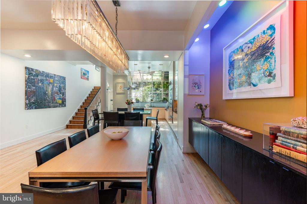 Dining area with a long wooden table, sculptural chandelier, colorful artwork, and hardwood floors.