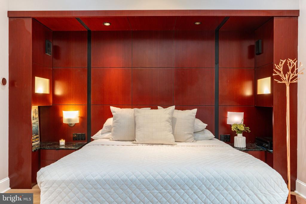 Bedroom with a white bed framed by a red-brown wood-paneled headboard and built-in bedside niches.