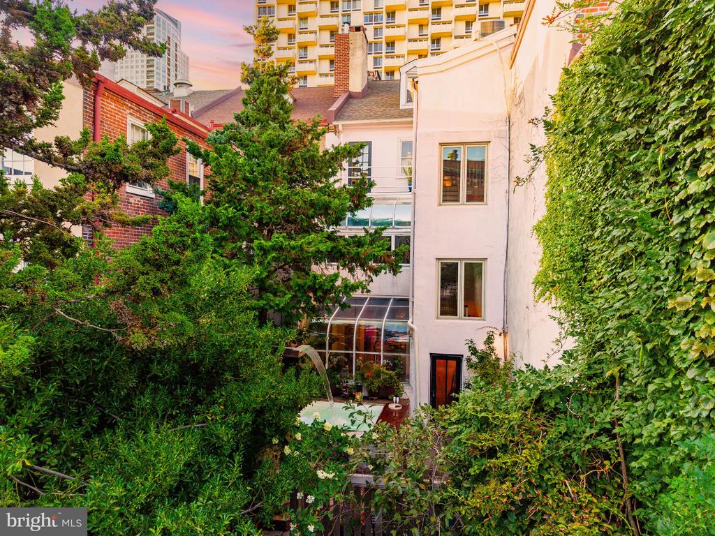 Rear courtyard of a multi-story home with a small pool, dense greenery, and a pale stucco facade.
