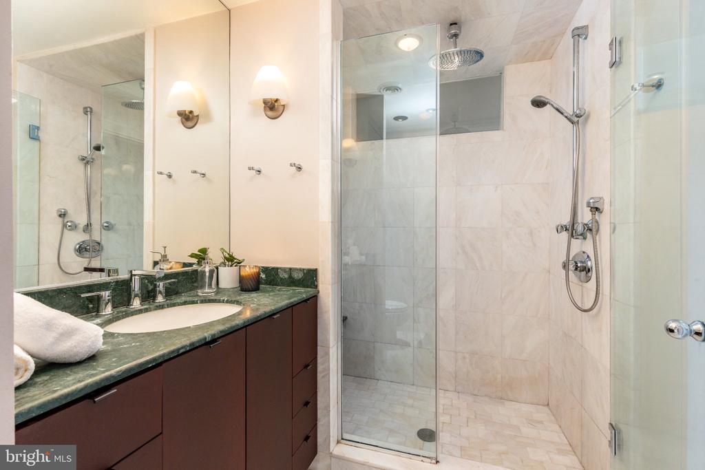 Marble bathroom with a green stone vanity and glass-enclosed shower with a rainfall showerhead.