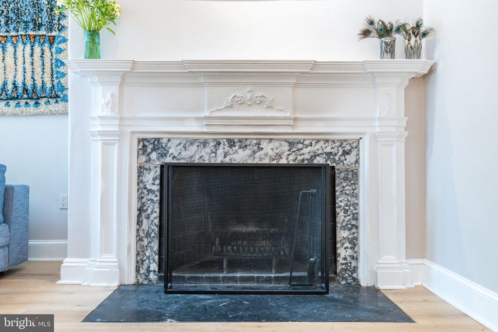 Ornate white living room fireplace with a marbled surround and dark fire screen.