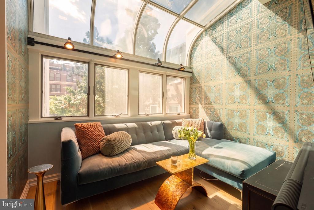 Sunroom with a curved glass ceiling, patterned teal tile walls, and a gray sectional sofa.