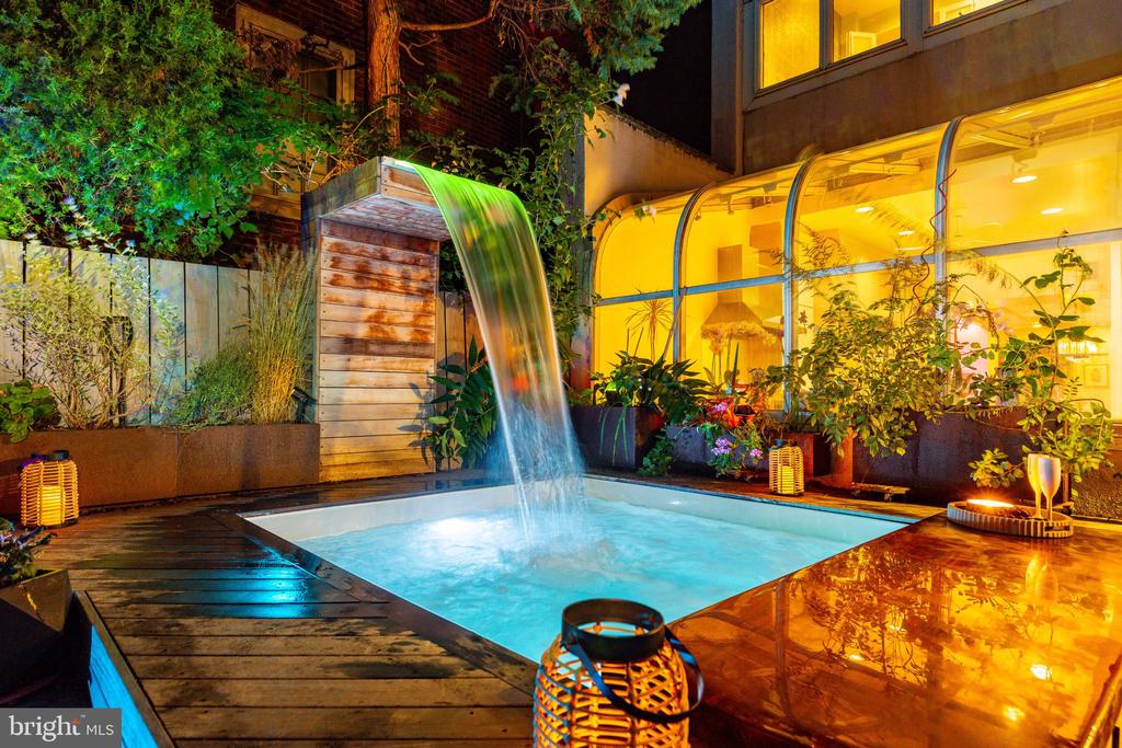 Outdoor pool with a wooden waterfall feature and warmly lit curved glass windows at night.