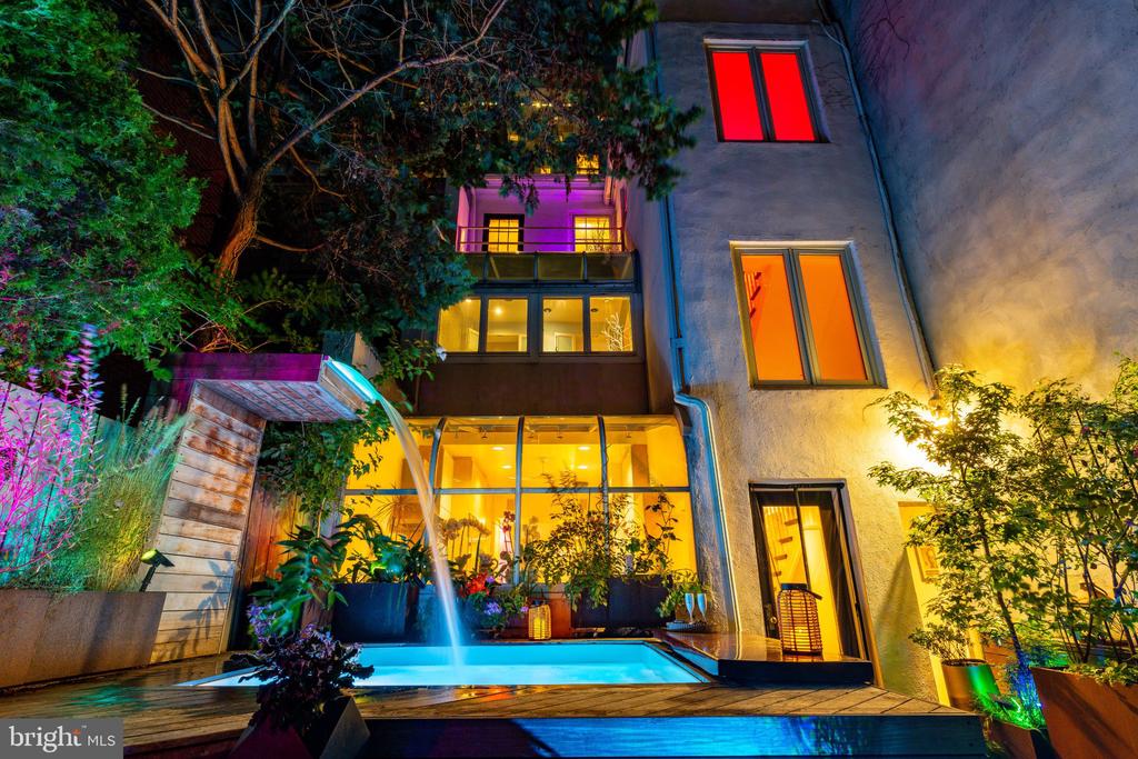 Multi-story home exterior at night overlooking an illuminated courtyard pool with a cascading waterfall.