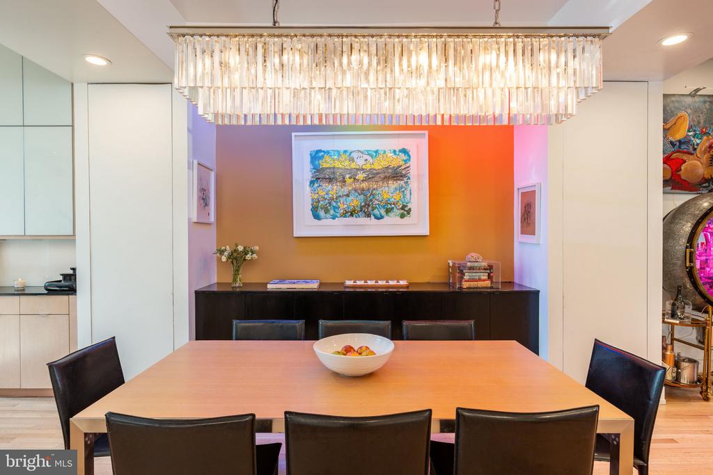 Dining room with a wooden table, black chairs, crystal chandelier, and colorful artwork.