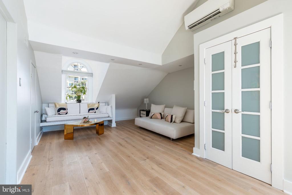 Living room with pale wood floors, a sloped ceiling, arched window, and white frosted-glass French doors.