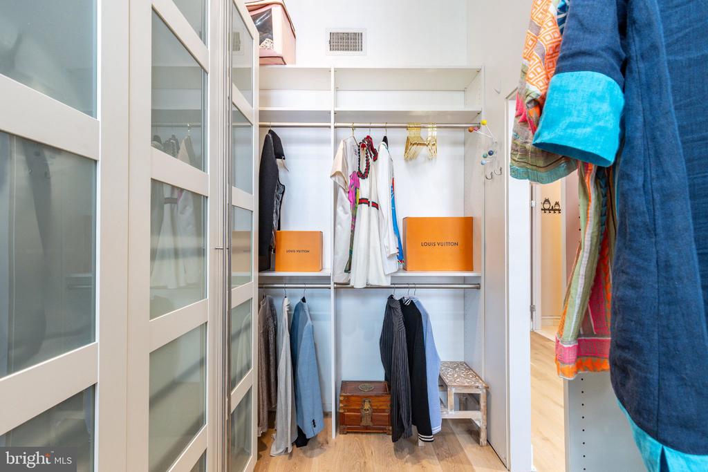 Walk-in closet with frosted-glass doors, white shelving, hanging clothes, and Louis Vuitton boxes.